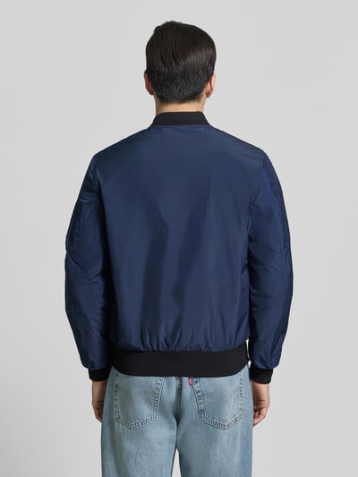 Męski model nosi Bomberjacke mit Label-Patch und Eingrifftaschen od Original Bombers, granatowy kolor, prosty krój, widok całej sylwetki od tyłu