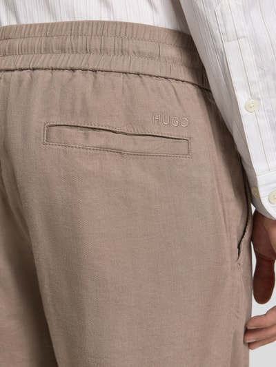 Mężczyzna nosi Straight Fit Chinoshorts aus Leinen-Lyocell-Mix Modell 'CINO' od HUGO, beżowy, flammgarn, haftowane logo, detal, zbliżenie tylnej części.