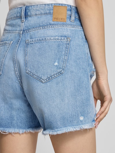 Kobiece model nosi Regular Fit Jeansshorts aus reiner Baumwolle Modell 'SUMMER' von Pieces, efekt znoszenia, splot twill, 5 kieszeni, naszywka z logo, zapięcie na guzik i ukryty zamek błyskawiczny, bawełna, denim stylizowany na jasny, widoczna faktura, gładka powierzchnia, detal szlufek na pasek, Ganzkörperansicht Rückansicht.