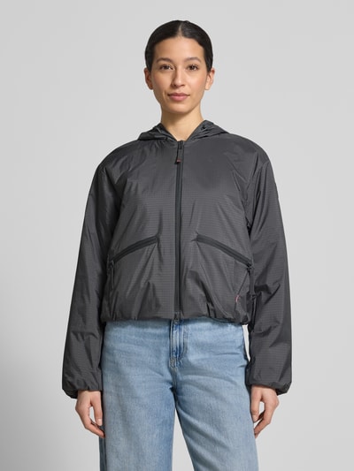 Kobiece modelka nosi szarą kurtkę z kapturem Jacke mit Reißverschlusstaschen Modell 'YADIRA' od FIRE + ICE, krój regular fit, z dwiema kieszeniami na zamek, długość tyłu w rozmiarze 36: 52 cm, szerokość ramion 45 cm, szerokość w rozmiarze 36: 45 cm, długość rękawa 61 cm, pełen widok z przodu.