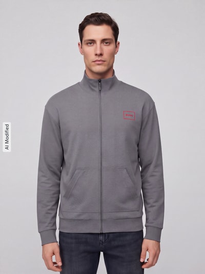 Męski model nosi szarą bluzę rozpinaną Regular Fit Sweatjacke aus Baumwoll-Mix model 'Laze Zip Jacket' od HUGO, widok całej sylwetki z przodu, bluza rozpinana HUGO, KI-modifiziertes Bild.