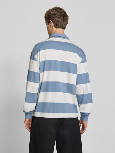 Männermodel trägt Relaxed Fit Poloshirt aus reiner Baumwolle von Champion, blau-weiß gestreift, glatte Struktur, Ganzkörperansicht Rückansicht.