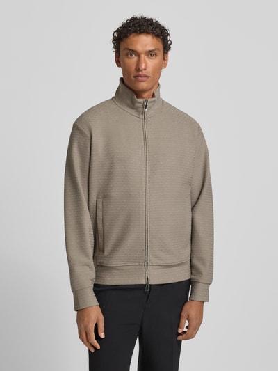 Männermodel trägt Sweatjacke mit Stehkragen von Emporio Armani in Beige, Baumwoll-Lyocell-Mix mit Stretch-Anteil, lockerer Schnitt, Reißverschluss, Eingrifftaschen, gerippte Abschlüsse, Rückenlänge 64 cm, Ärmellänge 60 cm, Ganzkörperansicht von vorne.