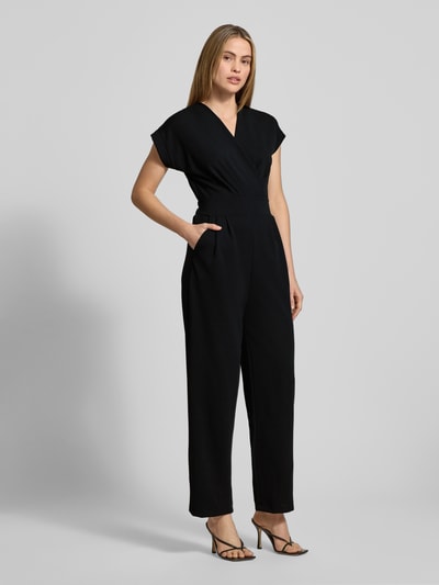 Frauenmodel trägt schwarzen Jumpsuit mit V-Ausschnitt und Eingrifftaschen, Modell 'Ko44a' von ZABAIONE, Material-Mix mit Stretch-Anteil, Regular-Fit, Ganzkörperansicht von vorne.