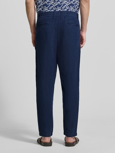Männermodel trägt Tapered Fit Leinenhose mit Eingrifftaschen van MCNEAL in donkerblauw, steekzakken, paspelzakken achter, tapered fit, zuiver linnen, bandwijdte maat M 45 cm, binnenbeenlengte maat M 76 cm, ganzkörperansicht rückansicht.