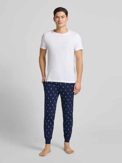 Mannelijk model draagt Sweathose mit Allover-Logo-Print van Polo Ralph Lauren in donkerblauw met witte logo's, losjes fit, elastische tailleband met trekkoord, contrastboorden, labelpatch, lengte binnenbeen maat M 69 cm, volledige lichaamsvoorzijde.