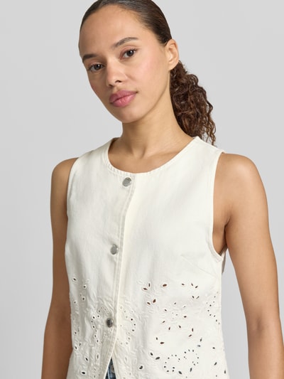 Frauenmodel trägt Weste mit Lochstickerei Modell 'JOANA' von Mango aus reiner Baumwolle in Offwhite mit Druckknopfverschluss, Nahaufnahme Oberkörper.