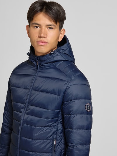 Männermodel trägt Regular Fit Jacke in Stepp-Optik Modell 'KINGSLEY' von JACK & JONES, marineblau, Kaptur, zamek błyskawiczny, wpuszczane kieszenie, Długość tyłu w rozmiarze M: 70 cm, Szerokość ramion w rozmiarze M: 45 cm, Szerokość klatki piersiowej w rozmiarze M: 52 cm, Długość rękawów w rozmiarze M: 67 cm, z efektem pikowania, Ganzkörperansicht von vorne