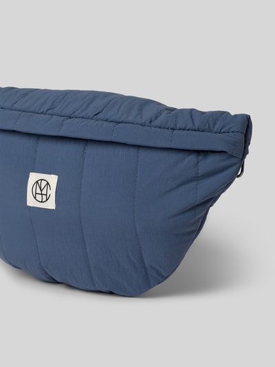 Produktfoto, Bauchtasche mit Label-Detail Modell 'SASJA' von MSCH Copenhagen in Blau mit Steppnähten, strukturierte Oberfläche, Nahaufnahme, Hauptfach mit Reißverschluss, Maße: 35x20x8 cm, Schulterriemen 81 cm.