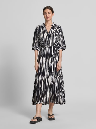 Frauenmodel trägt Hemdblusenkleid aus Viskose-Mix mit Knopfleiste Modell 'Salma' von GUIDO MARIA KRETSCHMER WOMAN, taillierter Schnitt, Midikleid mit Hemdblusenkragen, Bindegürtel, Rückenlänge 131 cm, Brustweite 46 cm, Ärmellänge 39 cm, schwarz-weiß gemustert, fließende Textur, Ganzkörperansicht von vorne.