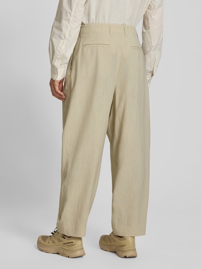 Männermodel trägt Stoffhose aus Viskose-Leinen-Mix von MAISON KITSUNÉ in Beige, Balloon Fit, Kellerfalten, Produktdetails sichtbar, Ganzkörperansicht Rückansicht.