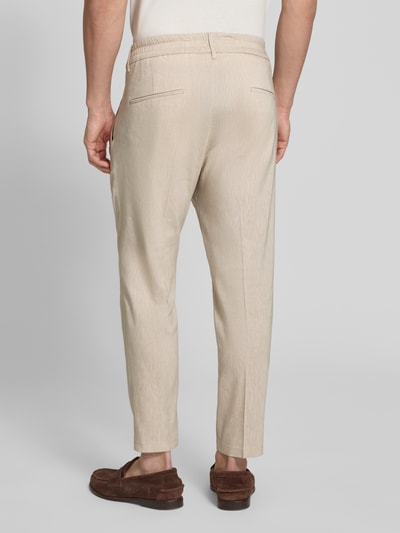 Męski model nosi Hose mit Bügelfalte und elastischem Bund Modell 'CHASY' od Drykorn, jasny beż, len z wiskozą, krój slim fit, szerokość w rozmiarze 32/32: 44 cm, długość nogawki wewnętrznej: 66 cm, widok całej sylwetki z tyłu.