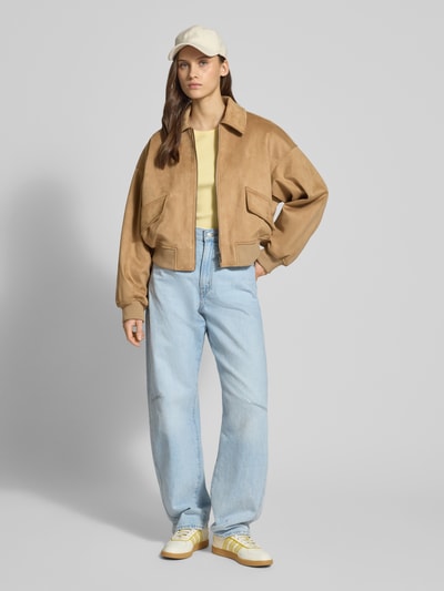 Kobiece modelka ma na sobie Regular Fit Bomberjacke mit Umlegekragen od Guess Jeans, beżowo-żółte odcienie, pełny widok z przodu. Szerokość w rozmiarze S: 45 cm, długość tyłu: 47 cm, szerokość ramion: 56 cm, długość rękawa: 40 cm, elastyczne wykończenia, zamek błyskawiczny.