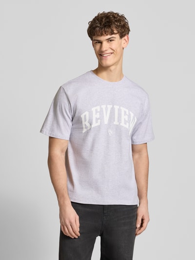 Männermodel trägt T-Shirt mit Label-Print und Rundhalsausschnitt von REVIEW aus reiner Baumwolle in Hellgrau, Regular Fit, Ganzkörperansicht von vorne.