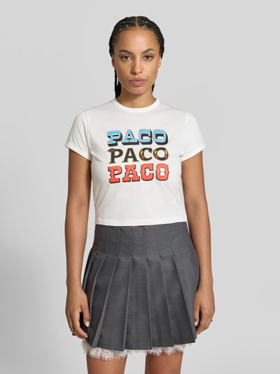 Frauenmodel trägt Regular Fit T-Shirt mit Statement-Print von Rabanne in Weiß aus reiner Baumwolle, Rundhalsausschnitt, kurze Ärmel, kombinierbar mit grauem Faltenrock, Ganzkörperansicht von vorne.