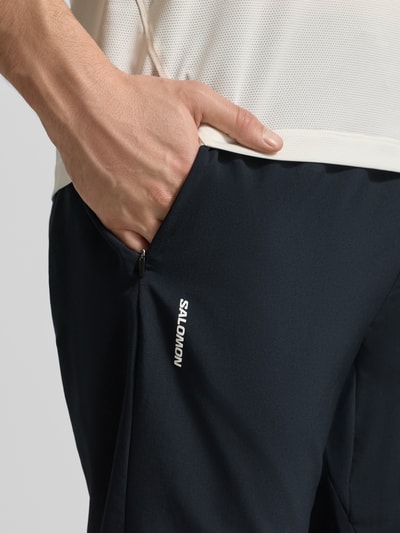 Männermodel trägt Trainingshose mit Logo und elastischem Bund von Salomon in Schwarz, Regular Fit, Nahaufnahme Oberschenkel.