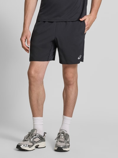 Männermodel trägt schwarze Regular Fit Shorts mit integriertem Slip Modell 'Core' von ASICS TIGER, Logo-Print, Ganzkörperansicht von vorne. Herren Shorts, elastischer Bund, Bundweite 38 cm, Innenbeinlänge 17 cm.