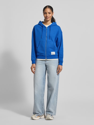 Frauenmodel trägt Sweatjacke mit Zweiwege-Reißverschluss von Smith and Soul, Relaxed Fit, Känguru-Tasche, Blau, Ganzkörperansicht von vorne.