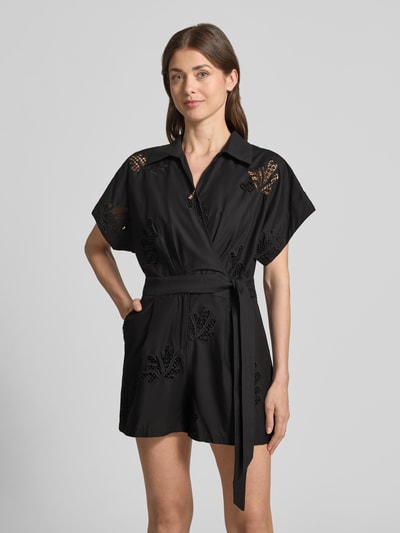 Frauenmodel trägt schwarzen Damen Jumpsuit in Wickel-Optik Modell 'TRACY' von SUNCOO PARIS aus Reine Baumwolle, Relaxed-Fit, Lochstickerei, Hemdblusenkragen, Bindegürtel, Ganzkörperansicht von vorne.