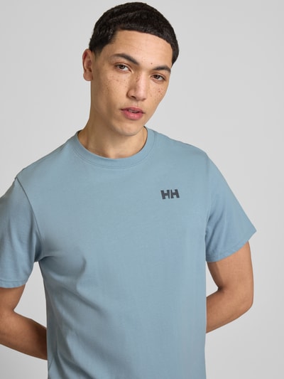 Männermodel trägt T-Shirt mit Logo- und Motiv-Print Modell 'SHORELINE' von Helly Hansen in Blau, Reine Baumwolle, Gerader-Schnitt, Rundhalsausschnitt, Nahaufnahme Oberkörper. Rückenlänge bei Größe M: 70 cm.