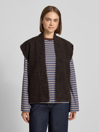 Modelka kobieca nosi czarną kamizelkę z imitacji futerka Regular Fit Weste in Teddy-Optik Modell 'NAYA' od ONLY na pasiastą bluzkę, widok całej sylwetki z przodu.