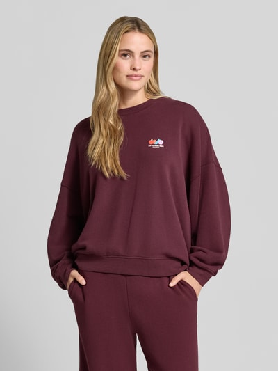 Frauenmodel trägt Oversized Fit Sweatshirt aus Baumwoll-Mix mit Stretch-Anteil von American Vintage, bordeaux, Motiv-Print, Rundhalsausschnitt, elastische Bündchen, Nahaufnahme Oberkörper.