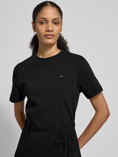 Vrouwenmodel draagt Tailliertes Sweatkleid aus reiner Baumwolle van Tommy Hilfiger in zwart, korte mouwen, logo-stitching, ceintuur, mini lengte, interlock van puur katoen, unicolor design. Close-up bovenlichaam.