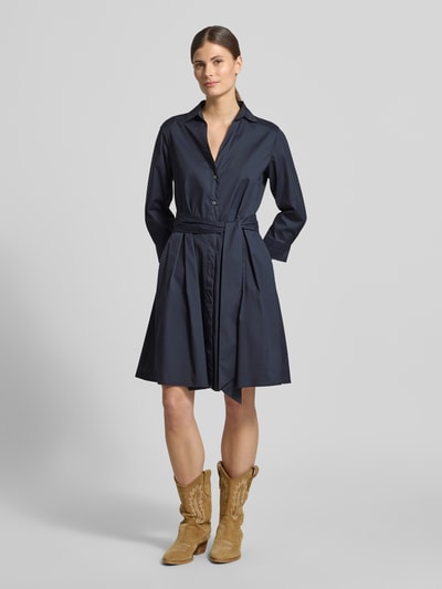 Modelka nosi Hemdblusenkleid mit Bindegürtel Modell 'JULE' von 0039 Italy, ciemnogranatowy bawełniano-elastyczny materiał, linia A, długość do kolan, dekolt V, pasek, długość pleców w rozmiarze S: 97 cm, szerokość w rozmiarze S: 49 cm, długość rękawa w rozmiarze S: 50 cm, całkowity widok z przodu.