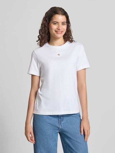 Frauenmodel trägt Regular Fit T-Shirt aus reiner Baumwolle von Calvin Klein Jeans in Weiß, schlichte Optik, kombiniert mit blauer Jeans, Ganzkörperansicht von vorne.