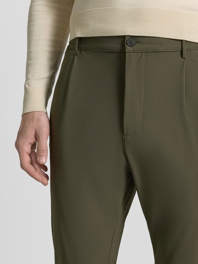 Męski model nosi Slim Fit Hose mit Paspeltaschen am Gesäß von CRUNA w kolorze oliwkowym, materiał z domieszką stretchu, eleganckie kieszenie boczne, szerokość w rozmiarze 50: 44 cm, długość nogawki wewnętrznej: 73 cm, krój slim fit, zbliżenie na górną część nóg i biodra.