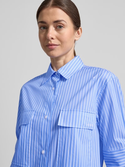 Modelka nosi sukienkę koszulową Relaxed Fit Hemdblusenkleid mit Brusttaschen Modell 'Daliya' od JOOP!, elastyczna mieszanka bawełny, kołnierzyk koszulowy, rękaw o dł. 1/2, nadruk z logo na całej powierzchni, listwa guzikowa, niebieskie i białe paski, szerokość w rozmiarze 36: 52 cm, długość tyłu w rozmiarze 36: 108 cm, długość rękawów w rozmiarze 36: 30 cm, półzbliżenie górnej części ciała.