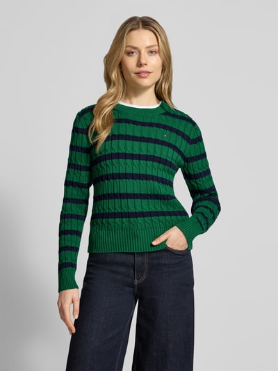 Frauenmodel trägt Slim Fit Strickpullover aus reiner Baumwolle von Tommy Hilfiger, grün-blau gestreift, Rundhals, langarm, Ganzkörperansicht von vorne.