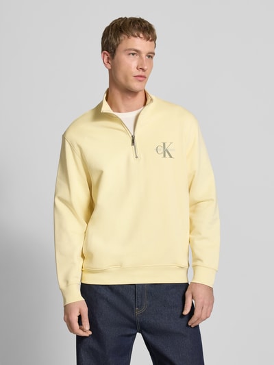 Männermodel trägt Sweatshirt mit Stehkragen und Reißverschluss von Calvin Klein Jeans aus Reine Baumwolle, Regular-Fit, Logo, hellgelb, Ganzkörperansicht von vorne.