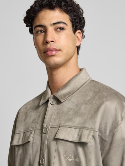 Männermodel trägt Relaxed Fit Hemdjacke mit Brusttaschen und Label-Stitching von Pegador aus Velours, Kentkragen, Knopfleiste, Nahaufnahme Oberkörper. Rückenlänge bei Größe M 70 cm.