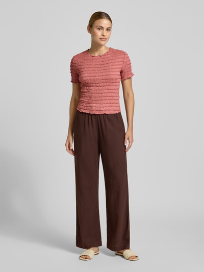 Frauenmodel trägt T-Shirt mit Strukturmuster und Rundhalsausschnitt von Jake*s Collection, Material-Mix mit Stretch-Anteil, Slim Fit, Rückenlänge bei Größe S 48 cm, in Altrosa, kombiniert mit brauner Hose, Ganzkörperansicht von vorne.