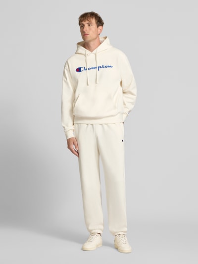 Männermodel trägt Sweatpants mit Label-Detail von Champion in Creme, gerader Schnitt, Baumwollmischung, Ganzkörperansicht von vorne.