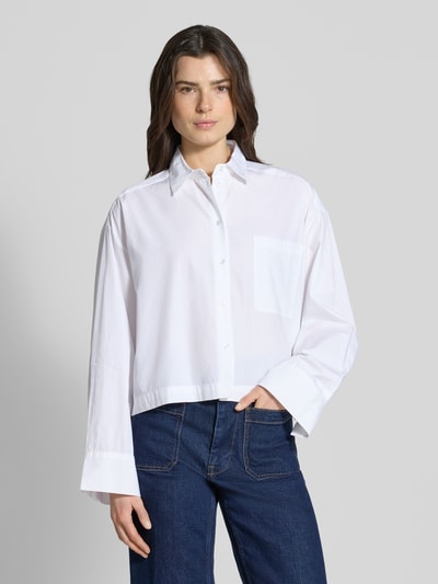 Frauenmodel trägt Oversized Hemdbluse aus reiner Bio-Baumwolle Modell 'Astha' von Selected Femme, weiß, mit Knopfleiste, Ganzkörperansicht von vorne.