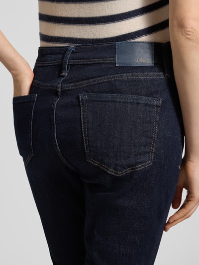 Frauenmodel trägt Bootcut Jeans aus Baumwoll-Mix von s.Oliver RED LABEL in Dunkelblau mit Label Patch, Denim-Struktur, Nahaufnahme Rückansicht.