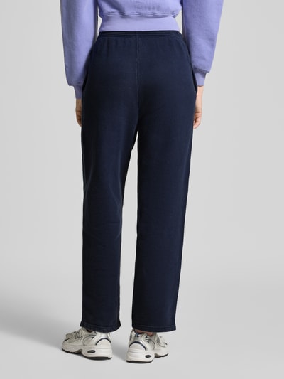 Frauenmodel trägt Sweatpants mit Label-Print Modell 'PLIZZY' von American Vintage aus reiner Baumwolle im Relaxed-Fit, Farbe Dunkelblau, elastischer Bund, Ganzkörperansicht Rückansicht.