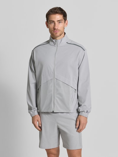 Männermodel trägt Regular fit heren jack met opstaande kraag Model 'Unstoppable' van Under Armour in lichtgrijs met elastische materiaalmix, elastische mouwboorden, ruglengte 67 cm, mouwlengte 64 cm, ganzkörperansicht van voren.