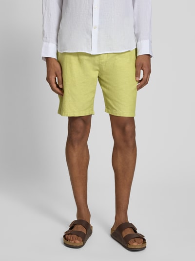 Męski model nosi szorty z elastycznym pasem od Scotch & Soda, mieszanka bawełny i lnu, krój regular fit, jasny żółty, tunel, szerokość w rozmiarze 32: 43 cm, długość wewnętrzna nogawki 20 cm, całkowity widok z przodu.
