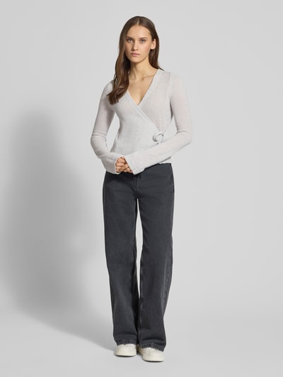 Frauenmodel trägt Strick-Cardigan in Wickeloptik von Review, V-Ausschnitt, Schleifenverschluss, lange Ärmel, Ganzkörperansicht von vorne.