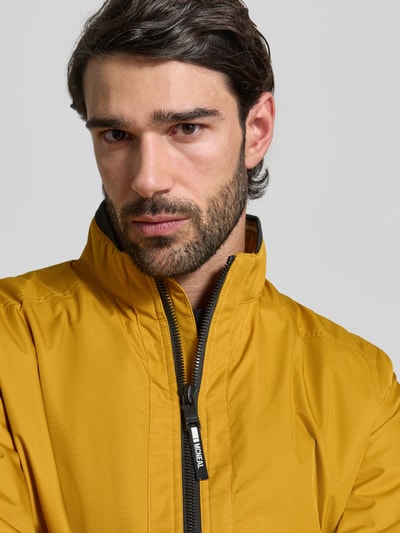 Männermodel trägt Regular Fit Jacke mit Stehkragen von MCNEAL in Gelb mit Reißverschluss, elastischen Abschlüssen, Nahaufnahme Oberkörper. Rückenlänge 64 cm, Schulterbreite 43 cm, Brustweite 55 cm, Ärmellänge 67 cm.