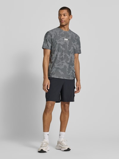 Mannenmodel draagt T-Shirt met Rundhalsausschnitt und Label-Detail van EA7 Emporio Armani, regular fit, grijs camouflagemotief, volledige lichaamsvoorzijde.