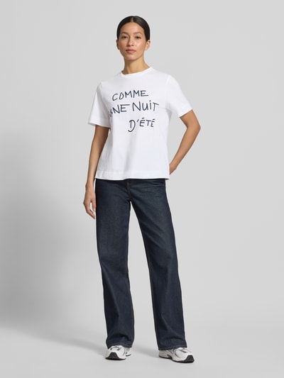 Frauenmodel trägt T-Shirt mit Statement-Print und Rundhalsausschnitt von Rich & Royal, Damen T-Shirt aus Reine Baumwolle im Relaxed-Fit, Rückenlänge 59 cm bei Größe S, weiß mit dunkelblauem Print, Ganzkörperansicht von vorne.