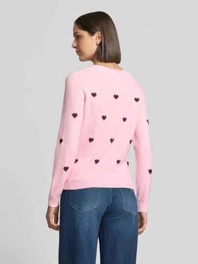 Frauenmodel trägt Regular Fit Pullover mit Rundhalsausschnitt Modell 'DOFFY' von VERO MODA in Rosa mit schwarzen Herzmotiven, Damen Pullover, Ganzkörperansicht Rückansicht.