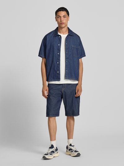 Männermodel trägt Modern Fit Jeanshemd mit Brusttasche Modell 'AUSTIN' von Jack & Jones aus gewachster Baumwolle, Ganzkörperansicht von vorne.