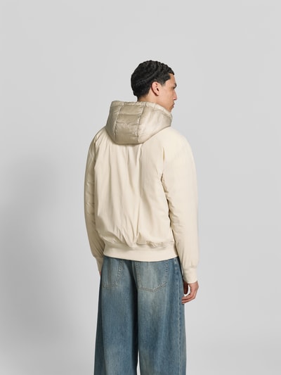 Männermodel trägt Bomberjacke mit Daunen-Feder-Füllung von Moose Knuckles in Beige mit Kapuze und Patten-Taschen, lockere Passform, Ganzkörperansicht Rückansicht. Rückenlänge bei Größe M: 63 cm, Schulterbreite: 48 cm, Ärmellänge: 65 cm.