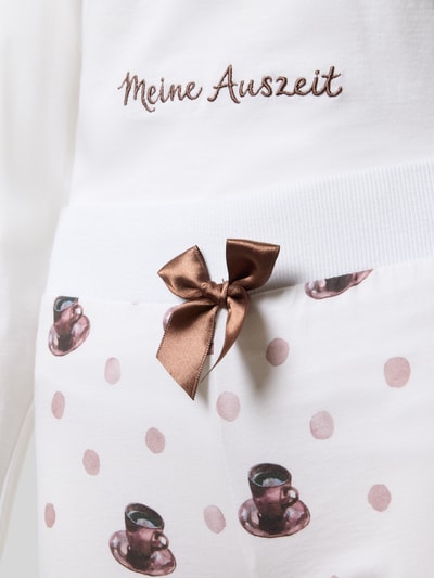 Frauenmodel trägt Regular Fit Pyjama aus reiner Baumwolle Modell 'Meine Auszeit' von LOUIS & LOUISA, weiß mit rosa Punkten und brauner Schleife, Nahaufnahme Oberkörper, Statement-Stitching und Allover-Motiv-Print sichtbar.