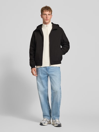Männermodel trägt Regular Fit Jacke mit Kapuze Modell 'Charge' von JACK & JONES, Schwarz, Reißverschluss, Ganzkörperansicht von vorne. Rückenlänge 68 cm, Schulterbreite 50 cm, Brustweite 60 cm, Ärmellänge 66 cm.